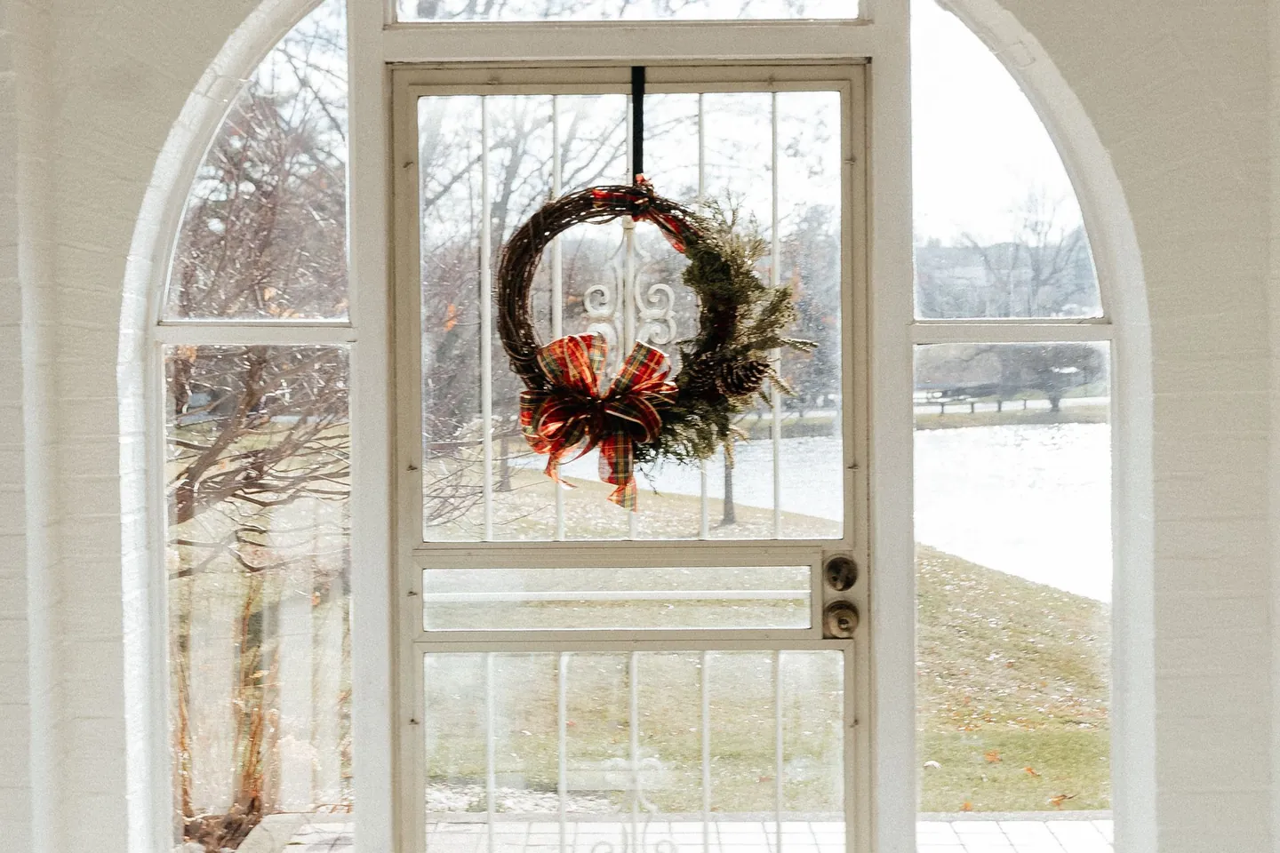 Holiday wreath hanging on the glass door of a bright home entry.