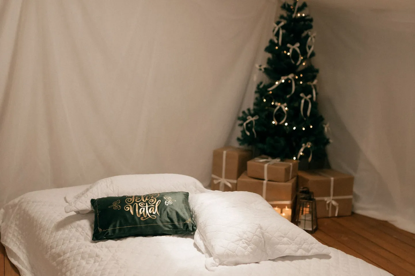 White bed with green pillows and a small Christmas tree.
